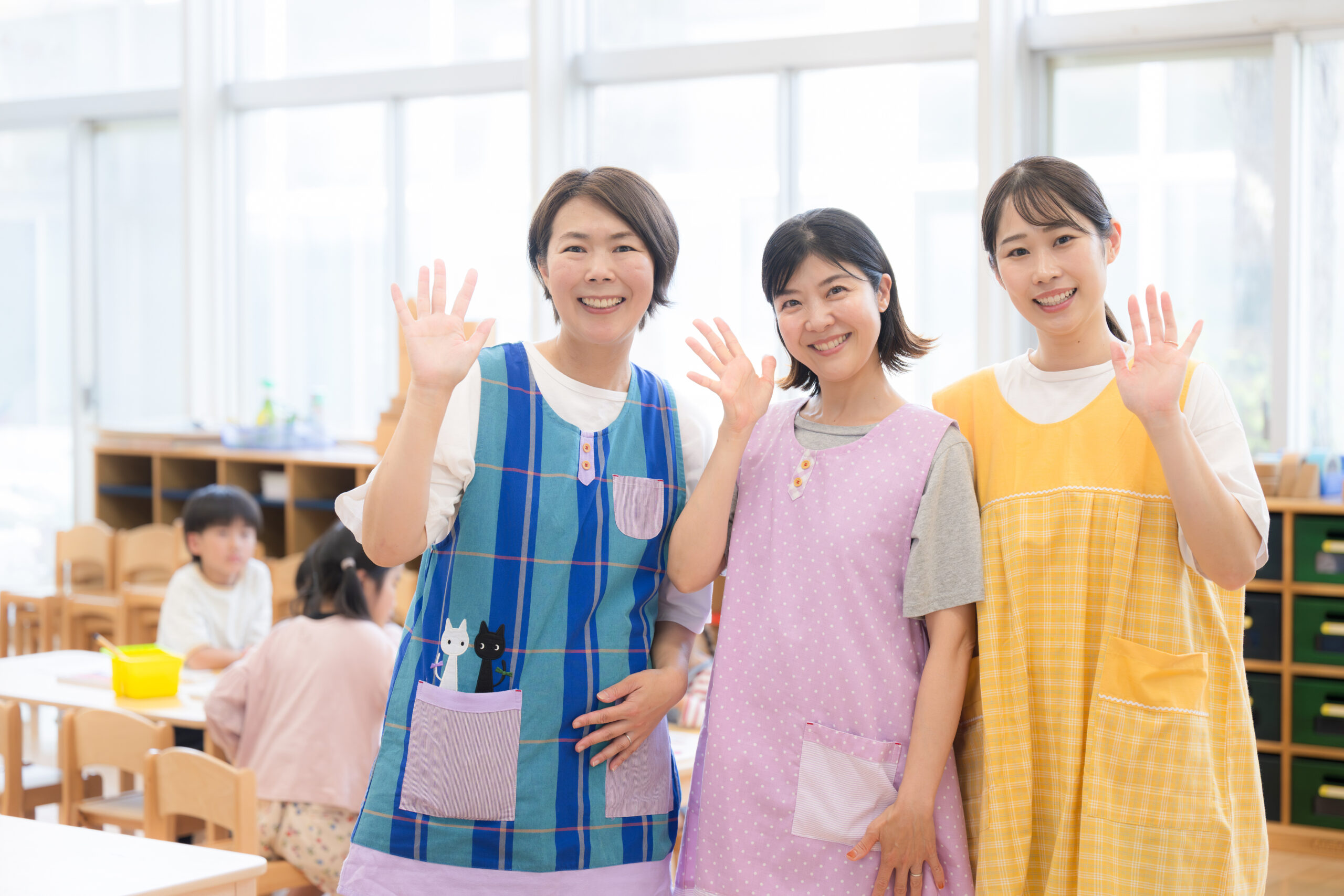 保育園や学童の保育士や先生の手を振る(バイバイ)イメージ　若い先生とベテラン先生のカメラ目線複数